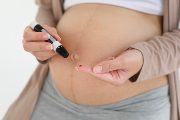 Photo une femme enceinte contrôle le taux de sucre dans le sang à l'aide d'un glucomètre numérique