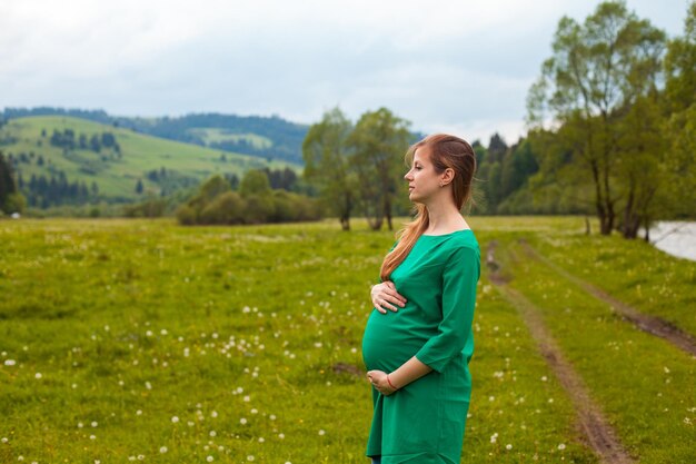 La femme enceinte dans une belle tunique verte respire l'air clair sur le fond de la nature avec des arbres verts