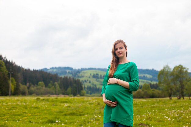 La femme enceinte dans une belle tunique verte respire l'air clair sur le fond de la nature