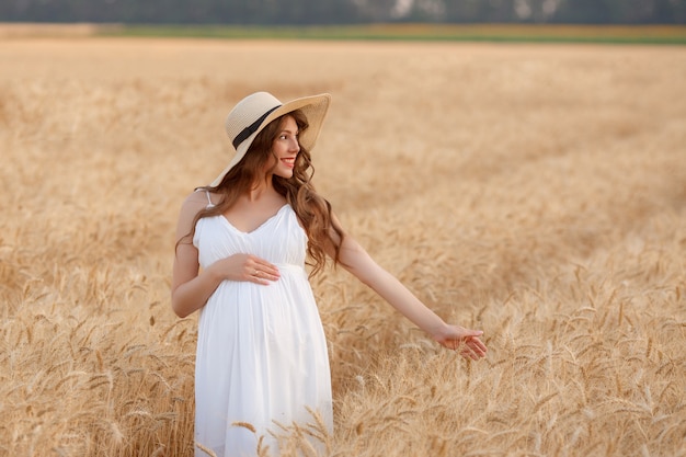 Femme enceinte dans un chapeau de paille dans un champ de blé