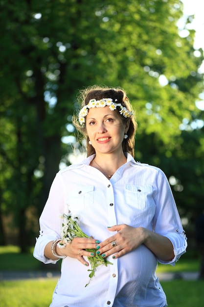 Femme enceinte dans une couronne et un bouquet de fleurs sauvages lors d'une promenade dans le parc