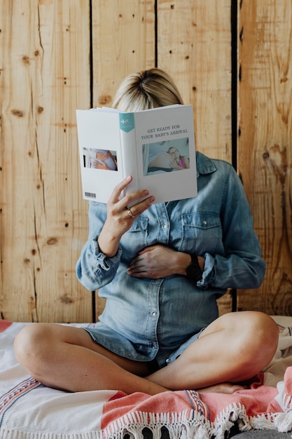 Femme enceinte dans une robe en jean lisant un livre sur un canapé