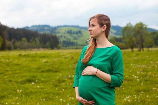 La femme enceinte dans une tunique verte respire l'air clair sur le fond de la nature