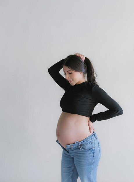 Une femme enceinte debout à côté de la fenêtre avec les mains sur le ventre