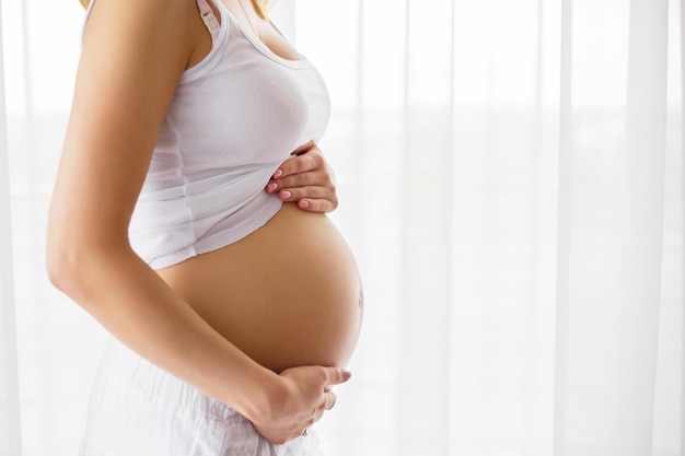 Femme enceinte debout à côté de la fenêtre