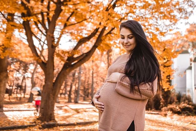 Femme enceinte debout dans la forêt du parc de la ville d'automne, tenant caressant son ventre rond avec bébé