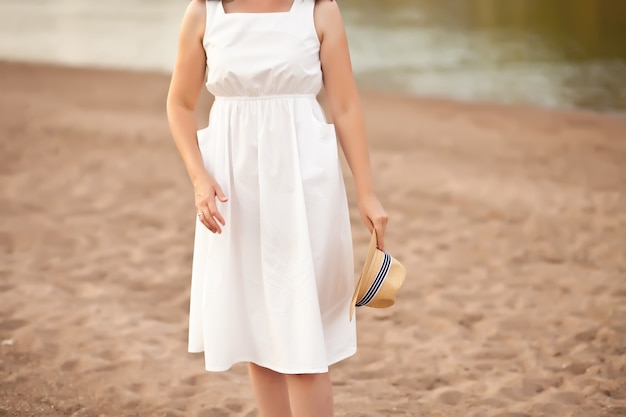 Femme enceinte debout sur la plage avec un chapeau dans une main