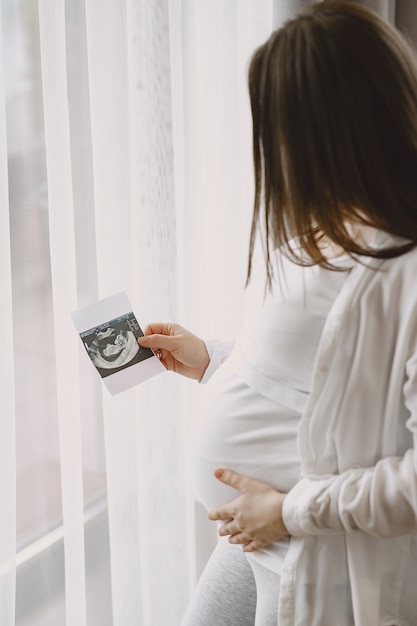 Photo femme enceinte debout près de la fenêtre en regardant une photo.