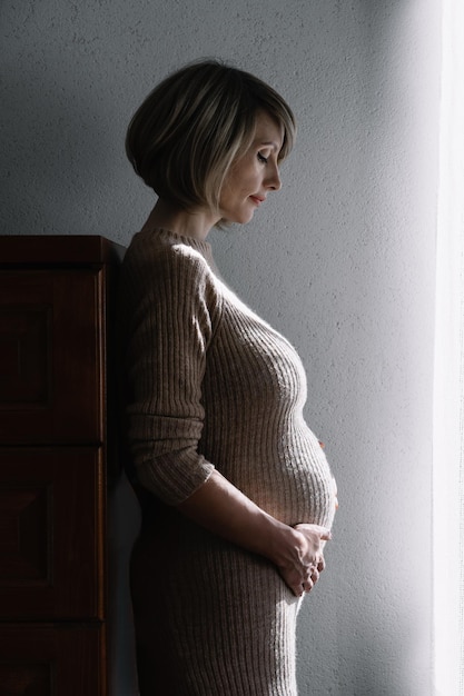 Une femme enceinte détournant son regard alors qu'elle se tient contre le mur à la maison