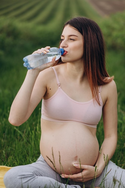 Femme enceinte de l'eau potable après la remise en forme assoiffé après l'entraînement femme enceinte gros plan espace libre sun light flare