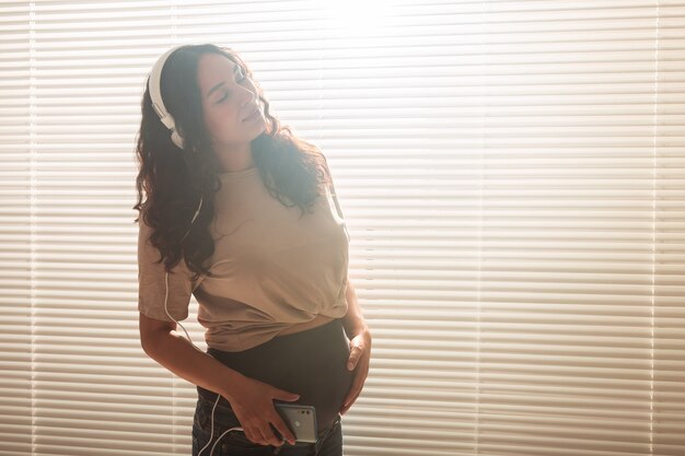 Une femme enceinte écoute de la musique dans des écouteurs à la maison et danse, copie l'espace.