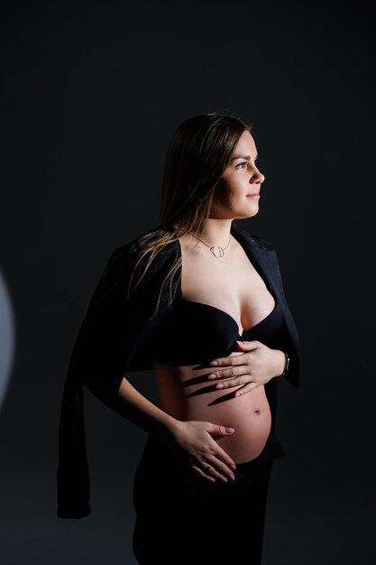 Femme enceinte élégante belle fille enceinte aux cheveux longs en costume noir sur fond gris concept de grossesse heureuse et de famille