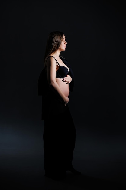 Femme enceinte élégante belle fille enceinte aux cheveux longs en costume noir sur fond gris concept de grossesse heureuse et de famille