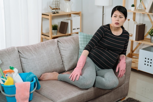 femme enceinte enceinte asiatique épuisée se frotte les jambes gonflées pour soulager la douleur tout en se reposant sur le canapé du salon avec les pieds nus après le ménage à la maison.