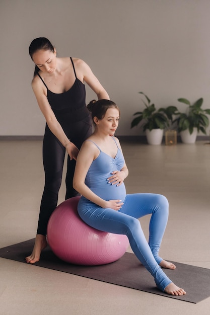 Femme enceinte avec un entraîneur pendant les cours de fitness avec un ballon