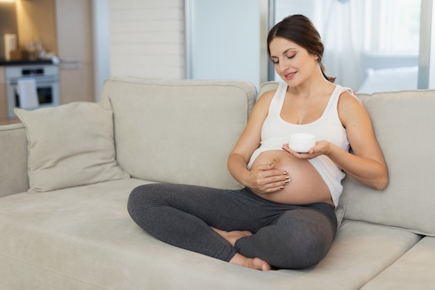 Une femme enceinte est assise à la maison sur un canapé léger