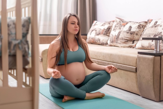 Une femme enceinte est assise à la maison en position du lotus et en vêtements de sport