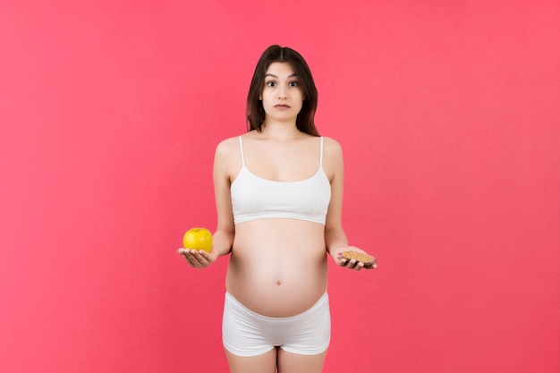 femme enceinte faisant un choix entre une pomme et un tas de pilules sur un fond coloré avec un espace de copie Prendre des vitamines pendant la grossesse concept