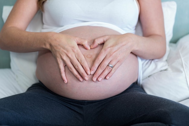 Femme enceinte faisant un coeur avec sa main sur son ventre dans sa chambre