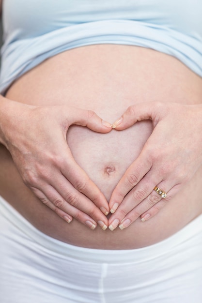Femme enceinte faisant un coeur avec sa main sur son ventre dans sa chambre