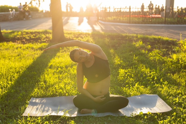 Femme enceinte faisant du yoga dans la nature à l'extérieur. Mode de vie sain, concept d'attente de bébé et de procréation.