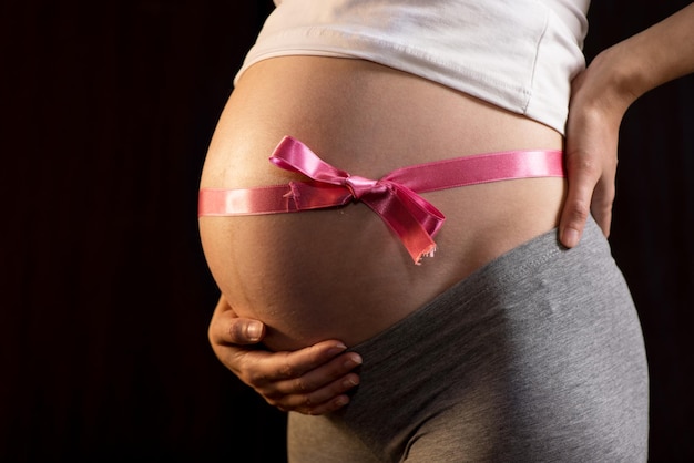 Femme enceinte sur fond noir avec ruban sur le ventre.