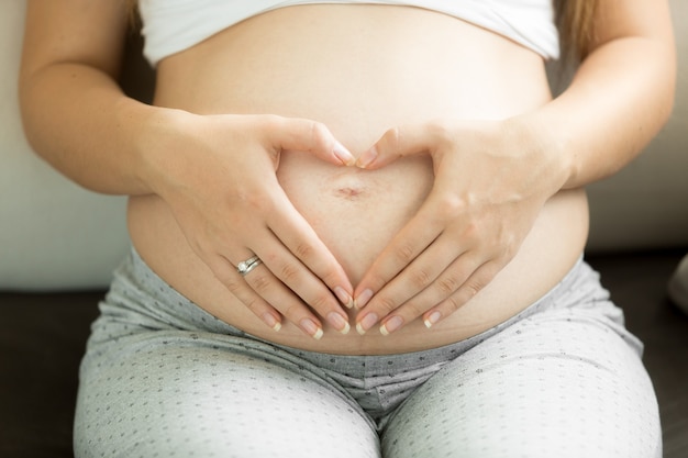 Femme enceinte en gros plan en forme de coeur avec les mains