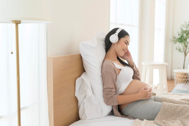 Une femme enceinte heureuse avec des écouteurs écoutant de la musique de Mozart et allongée sur le lit concept de grossesse