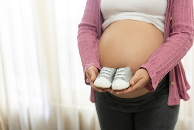 La femme enceinte heureuse tient des chaussures de bébé