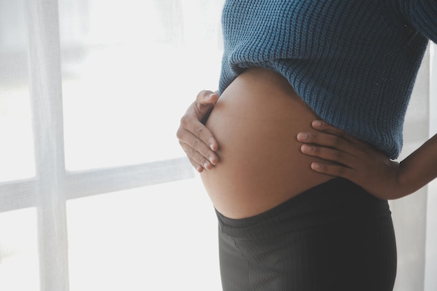 Une femme enceinte heureuse touchant son ventre devant un mur blanc.