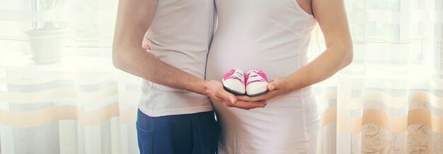 La femme enceinte et l'homme embrassent le ventre et tiennent des chaussures de bébé.