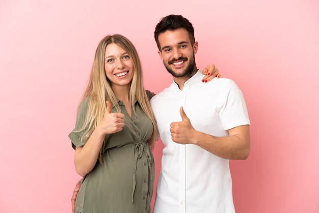 Femme enceinte et homme sur fond rose isolé donnant le geste du pouce vers le haut