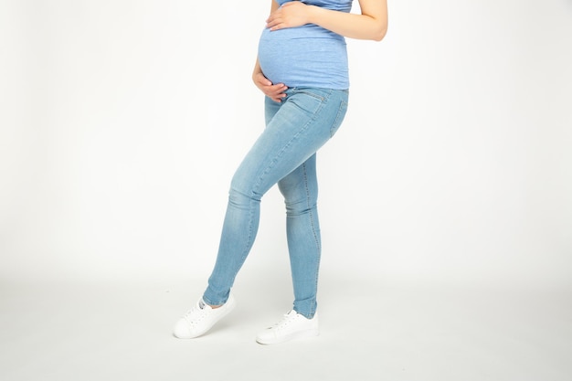 Une femme enceinte en jeans et débardeur tient son ventre.