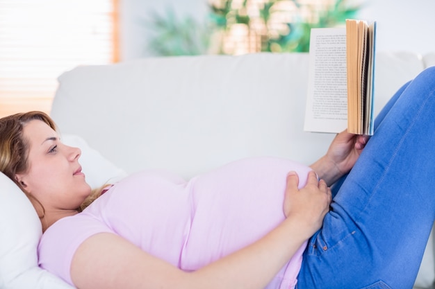 Femme enceinte en lisant un livre sur le canapé