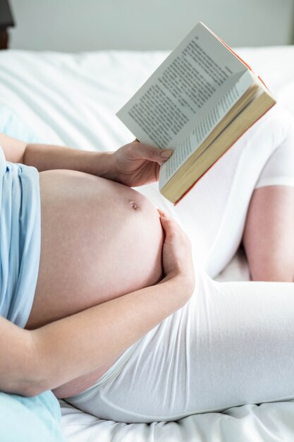 Femme enceinte sur un lit en lisant un livre à la maison