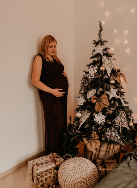 Femme enceinte en longue robe noire près de l'arbre décoré de Noël. Matin de noël. L'intérieur du nouvel an. Célébration de la Saint-Valentin