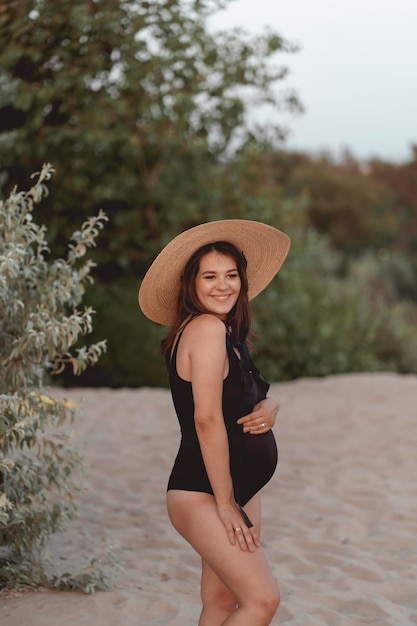 femme enceinte en maillot de bain noir et chapeau sur une plage de sable