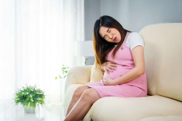 Une femme enceinte a mal au ventre sur un canapé dans le salon