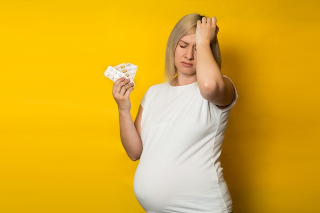 Une femme enceinte avec un mal de tête détient des pilules sur un mur jaune. médicaments sûrs pour la grossesse