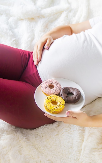 Une femme enceinte mange des beignets sucrés. Mise au point sélective.