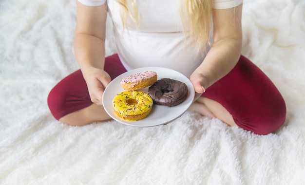 Une femme enceinte mange des beignets sucrés. Mise au point sélective.