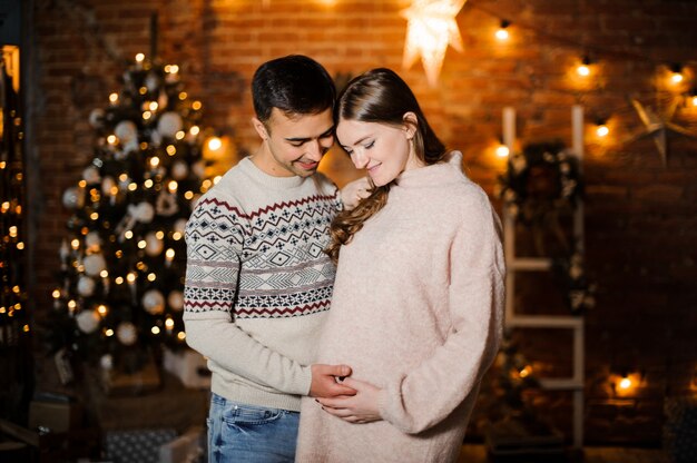 Femme enceinte avec mari debout sur le fond de l'arbre de Noël