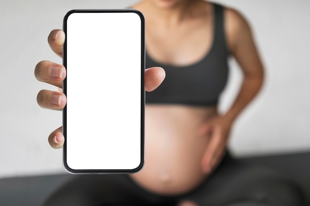 Femme enceinte méconnaissable démontrant un gros smartphone avec écran blanc vierge