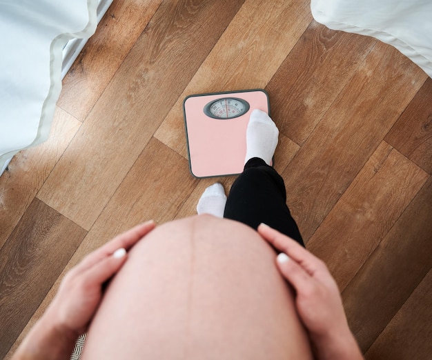 Femme enceinte méconnaissable avec un gros ventre abdomen regardant vers le bas tout en vérifiant le poids sur des balances électroniques mère recadrée avec le ventre inquiet de la figure pendant l'humeur de la maternité