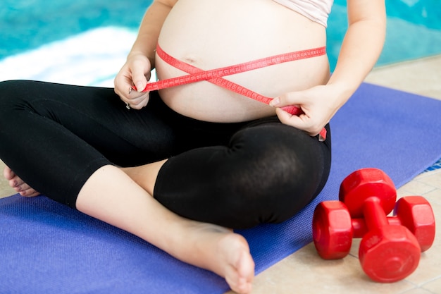 Femme enceinte mesurant son ventre sur un tapis de fitness bleu