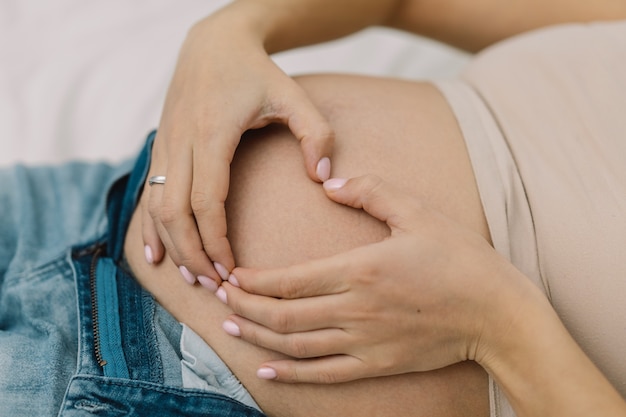 Une femme enceinte montre un cœur sur son gros ventre.