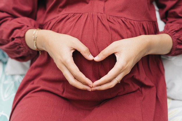 Photo une femme enceinte musulmane asiatique tenant son ventre créant un signe d'amour en utilisant les mains.