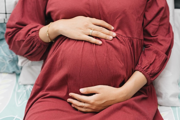 Une femme enceinte musulmane tenant son ventre pendant qu'elle est allongée sur le lit.