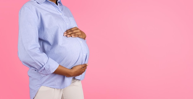 Une femme enceinte noire millénaire touche le ventre avec les mains et profite de la maternité isolée sur fond rose