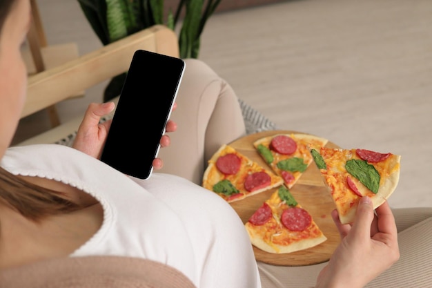 Une femme enceinte non reconnaissable dégustant une pizza tenant une délicieuse tranche et un smartphone avec un espace de copie d'affichage vide pour la publicité un espace vide pour la promotion